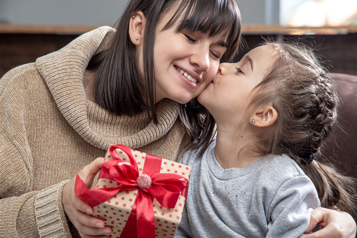 Little girl kisses mom holding a gift